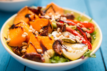 Healthy Paleo Salad with Pumpkin, Sweet Potato, Red Pepper and Nuts on Blue Wooden Background, Close-up
