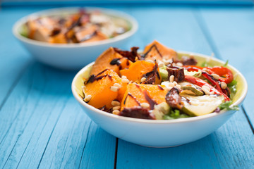 Healthy Paleo Salad with Pumpkin, Sweet Potato, Red Pepper and Nuts on Blue Wooden Background, Close-up