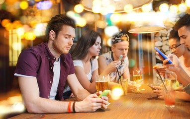 friends with smartphones and drinks at bar
