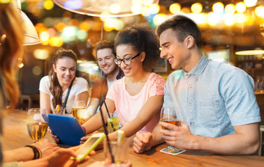 happy friends with tablet pc and drinks at bar