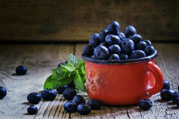 Ripe blueberries in red enamel mug, vintage wooden background, r