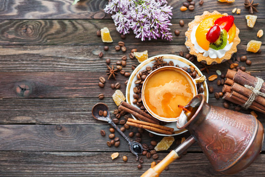 Rustic wooden background with cup and cezve of coffee, fruit tart and lilac flowers. White vintage dinnerware and spoon. Breakfast at summer morning. Top view, place for text.