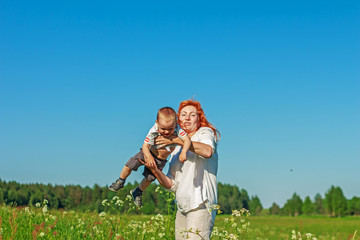 Beautiful red-haired mother playing with her baby in the field.