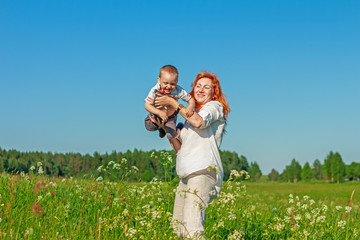 Beautiful red-haired mother playing with her baby in the field.