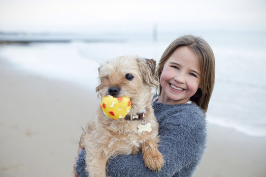 Young Girl Playing With Pet Dog And Ball On Beach
