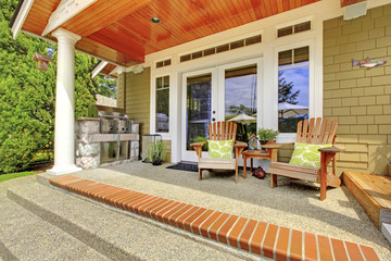 Countryside house exterior. View of column porch with chairs and concrete floor.