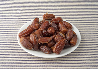 Tunisian pitted dates on a plate atop a blue striped tablecloth.