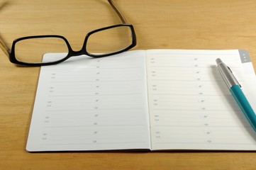 Wooden desk with address book, pen and reading glasses