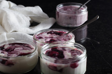Yogurts with fruits assortment in glass bowls on dark marble background. Natural and fruit healthy, diet, gourmet dessert for granola breakfast. Sweet yoghurts closeup.