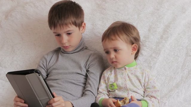 Children sitting on the couch playing on your tablet and phone to computer games