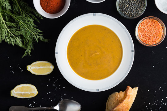 Cream soup of assorted lentil. Yellow and green lens, spices as raw for meal and lemon on black background. Healthy, appetizing, delicious, vegetarian food. Top view, copy space.