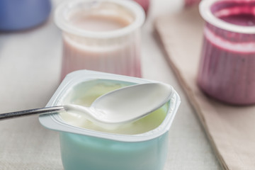 Yogurts assortment  in plastic bowls on light cloth background. Natural and fruit healthy, diet, gourmet dessert for granola breakfast. Sweet yoghurts closeup.
