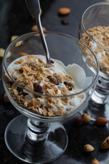 Granola with yoghurt, nuts and fruits in glass bowl on dark background. Delicious, healthy sweet dessert for breakfast. Cereal, muesli.  Copy space, closeup.
