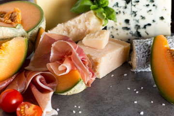 Jambon mix. Ham. Traditional Italian and Spanish salting, smoking, dry-cured dish - jamon Serrano and prosciutto crudo sliced with melon on grey background. Copy space. Closeup.