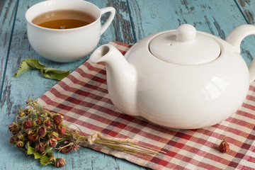   Tea. Teapot on a napkin, sprigs of the dried of wild strawberry and a cup of tea on a blue wooden background.