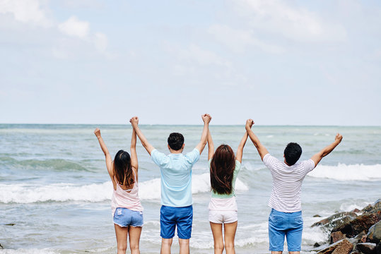 Rear view of young people standing at the beach and holding hands