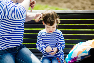 Young modern mother combing her small charming daughter on the bench in the park