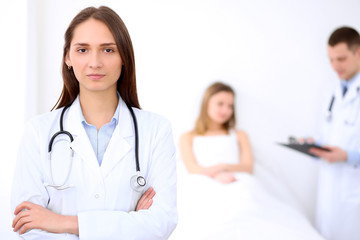 Fototapeta premium Friendly female doctor on the background with patient in the bed and his doctor