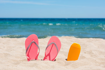 Fototapeta na wymiar Sunscreen bottle and pink flip flops on the beach