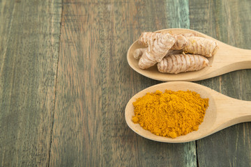 the turmeric powder in spoon and roots on wooden plate