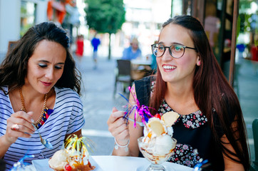 Smiling friends eating ice cream in outdoor cafe