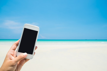 Woman hand hold white mobile phone with sea and blue sky