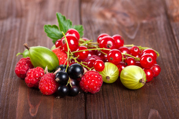 A mixture of ripe berries on a wooden table. Summer Still Life. Raspberries, gooseberries, currants close-up.