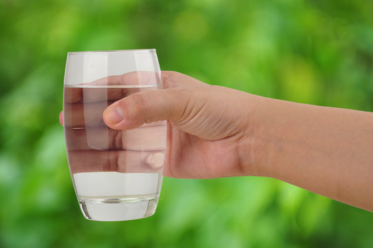 Hand Holding Glass of Water in Green Nature Background