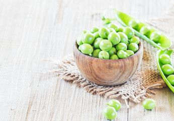 Fresh, young green peas in a wooden bowl, selective focus.