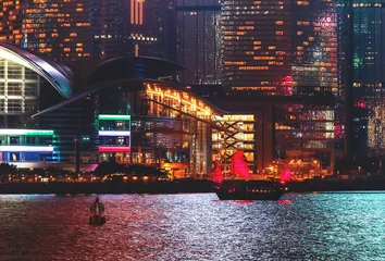Zelfklevend Fotobehang View over Hong-Kong, China, by night. Nighttime skyline with illuminated skyscrapers and the traditional junk boat. © Funny Studio