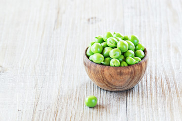 Fresh, young green peas in a wooden bowl, selective focus.