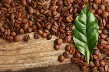 Coffee beans and green leaves on wooden background