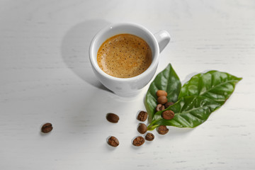 Cup of coffee with beans and leaves on light background