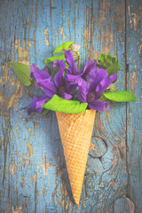 Bouquet of blue clematis in ice cream waffle cone on vintage bac