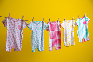 Baby clothes hanging on rope on yellow background