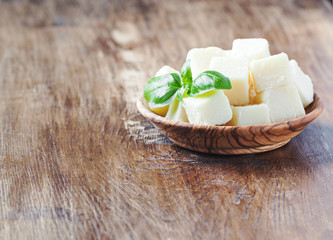 Parmesan cheese with basil in a wooden bowl on dark board. Selective focus.