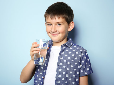 Cute boy drinking water on light background