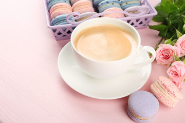 Cup of coffee with macaroons and roses on pink background