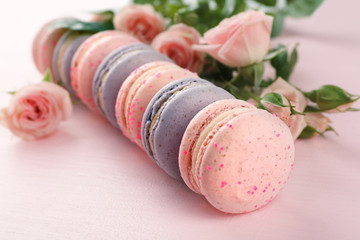 Tasty macaroons with beautiful roses on pink background