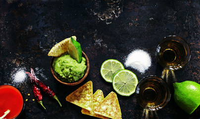 Tequila gold with sangrita chaser shots with lime slice with guacamole over old black metal surface, top view