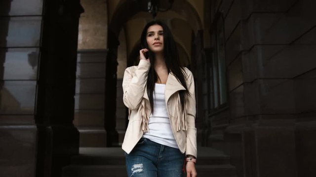 Fashion style portrait of young beautiful calm female model posing at city street with magnificent old architecture
