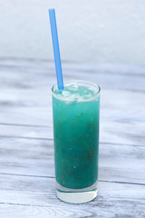 Blue lemonade in glass with ice and lemon on wood background