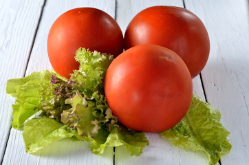 Red tomatoes and lettuce on a wooden table, saving a photo.