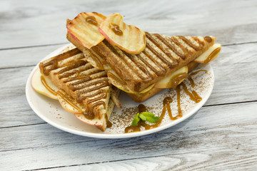 Sweet sandwich with caramel and grilled apple on wood background