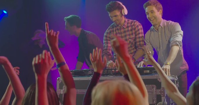 Man operating DJ machine and his friends dancing on music in nightclub