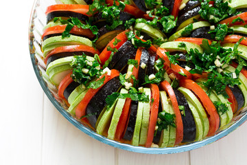 Raw Ratatouille with eggplants, tomatoes and zucchini decorated basil leaves on white wooden background
