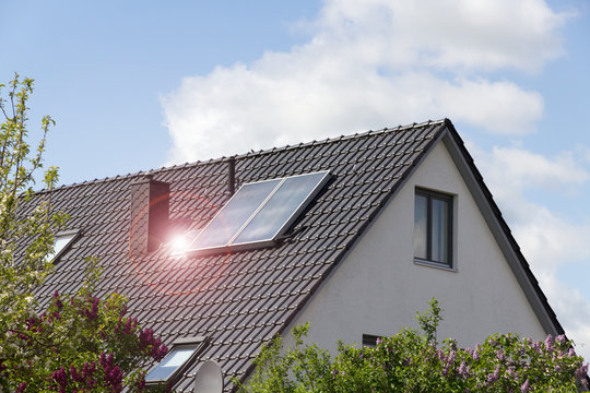 house with solar panels on the roof with blue sky and lens flare