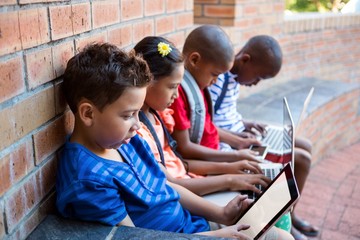 Students using dital tablet and laptop at school corridor