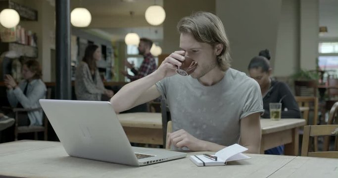 Man using laptop and drinking coffee in pub