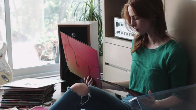 Young woman sitting nearby record player and changing record